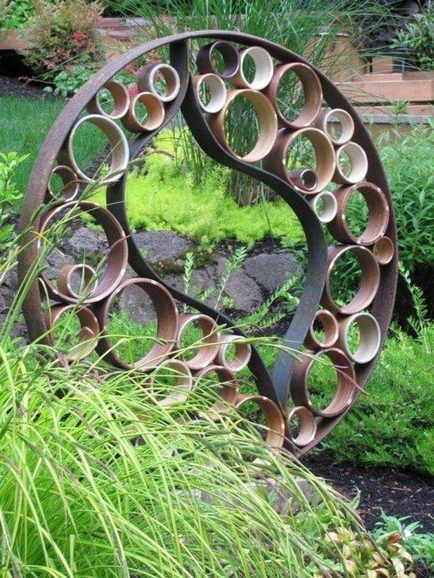 Large rusted circular metal garden sculpture with honeycomb ring pattern set among green foliage