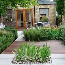 Landscaped backyard with stone patio, river-rock planter, wooden decking, and yellow-brick house with glass doors