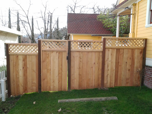 Light wood privacy fence with diamond lattice topper and matching gate beside a yellow house