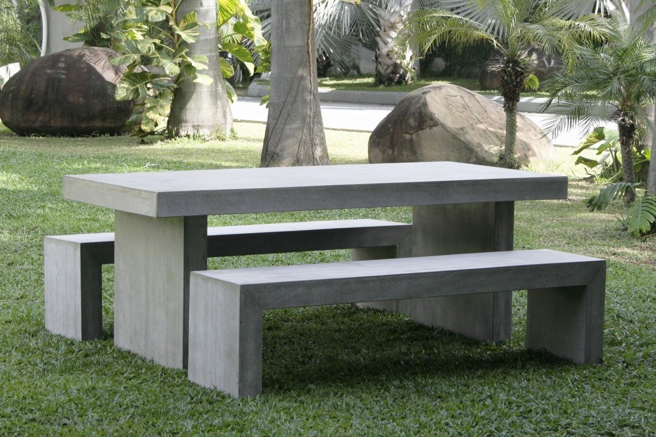 Light gray concrete outdoor dining table and matching benches on a green lawn among tropical plants
