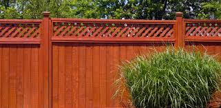 Reddish-brown stained wooden privacy fence with decorative lattice top and ornamental grass in front